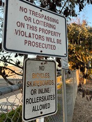 Two weathered signs display warnings against trespassing and the use of bicycles, skateboards, and...