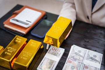 An Asian businesswoman sits at her desk analyzing gold bar prices, buying and selling gold, trading gold stocks, monitoring charts, and studying currency trends in an uptrending stock market.
