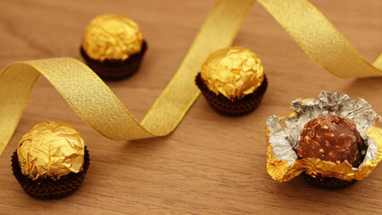 Gift background of chocolate truffles wrapped in silver paper and golden ribbon