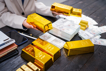 An Asian businesswoman sits at her desk analyzing gold bar prices, buying and selling gold, trading gold stocks, monitoring charts, and studying currency trends in an uptrending stock market.