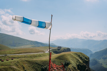A wind cone with white and blue stripes on the background of a mountain landscape. An outbuilding...
