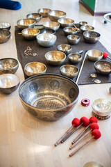 A collection of Tibetan singing bowls of various sizes placed on a mat, accompanied by wooden mallets and accessories, creating a serene and meditative ambiance