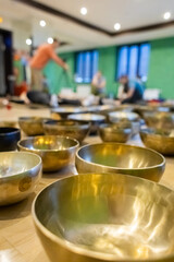 Close-up view of Tibetan singing bowls in a wellness studio with blurred background showing people engaging in a sound healing session or meditation activity