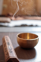 Ornate wooden incense holder releasing fragrant smoke next to a golden singing bowl, creating a peaceful atmosphere for meditation and relaxation on a wooden surface
