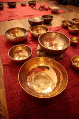 A close-up arrangement of brass singing bowls placed on red textured fabric, reflecting warm light and creating a serene and harmonious ambiance for sound healing practices