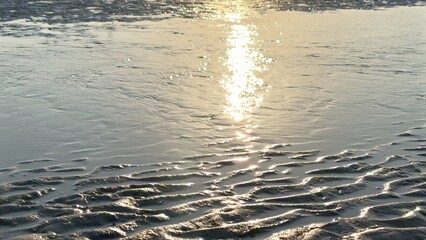 Tidal landscape and sand shimmer under soft golden sunlight, rippling patterns creating luminous reflections across serene coastal scenery, blending natural textures with tranquil oceanic hues.