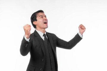 Excited and joyful young businessman wearing a formal black suit and tie, raising his fists in celebration of success and achievement, showing happiness and triumph, isolated on a white background