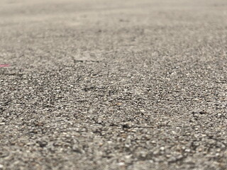 A close-up view of a textured asphalt surface, showcasing its roughness and small gravel particles.
