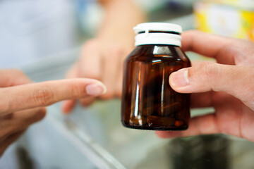 Photo of a pharmacist instructing a patient on how to store tablets in an opaque container in a pharmacy, Thailand.