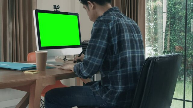 A man is sitting at a desk in front of a green computer monitor.