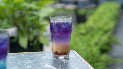 A glass of colorful two-tone drink, possibly a cocktail or refreshing beverage, sits on a textured...