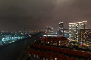 A new residential area of the Moscow capital Khoroshevo-Mnevniki and Filevsky Park with high-rise residential buildings and a view of the Moscow River with lights at night with a gloomy sky.