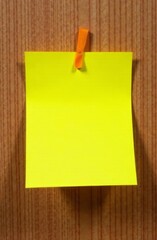 A bright yellow sticky note is attached to a wooden surface using an orange ribbon. The note is blank, creating a vibrant contrast with the natural wood, inviting thoughts and reminders.