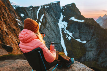Woman traveling in Norway sitting in camping chair drinking tea with thermos on mountain summit, girl hiking in Lofoten islands alone, adventure vacations getaway healthy lifestyle trip