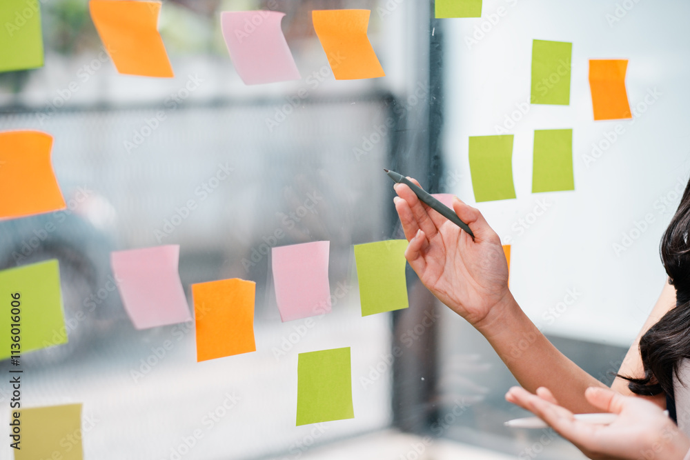 Poster hands arranging colorful sticky notes on a glass wall during a creative brainstorming session in a m