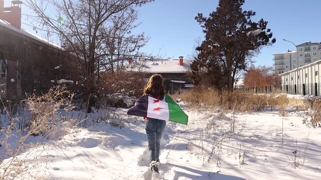 Young girl walks through the snow, draped in the Syrian Revolution Flag across her shoulders, filled with hope for a brighter and prosperous future for herself and all Syrians.
