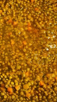 Italian traditional Christmas and festive meal: lentils with soffritto, slowly bubbling away in a pan. Real home cooking. Lentils are almost done. Vegetarian or vegan. Vertical video. 