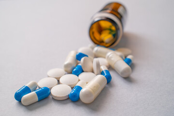 White and blue prescription pills and capsules spilling from prescription bottle, medical treatment...