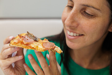 Happy woman eating a slice of pizza at the table in an Italian restaurant.