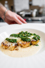 A beautifully plated dish featuring grilled cauliflower topped with a vibrant green pesto, sprinkled with cheese, and served on a creamy sauce. Ideal for food-related content.