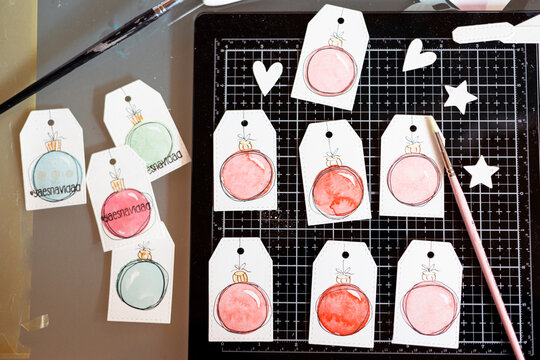 Overhead view of handmade Christmas gift tags with watercolour painted Christmas baubles and the words ya es navidad