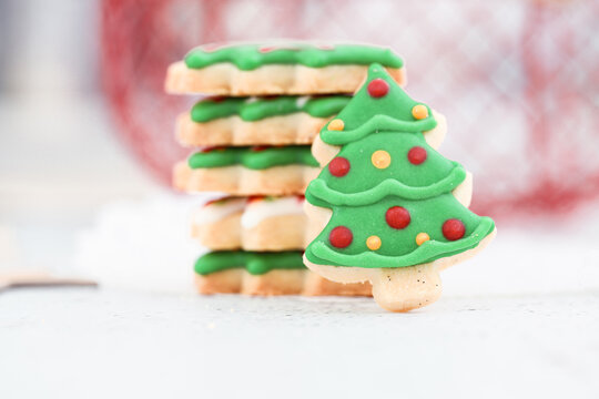 Close-up of a Christmas tree cookie with icing leaning against a stack of cookies on a table