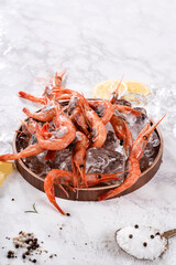 신선한 붉은 새우가 얼음과 함께 담긴 나무 그릇에 담겨 있으며, 옆에는 레몬 조각, 허브 잎, 그리고 소금이 놓여 있습니다. 대리석 바닥 위에 식재료가 깔끔하게 배치되어 고급스러운 분위기를 연출합니다.