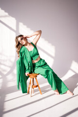 Kobieta w zielonym kombinezonie przy naturalnym świetle padającym z okna na drewnianym krześle © robertpstryka