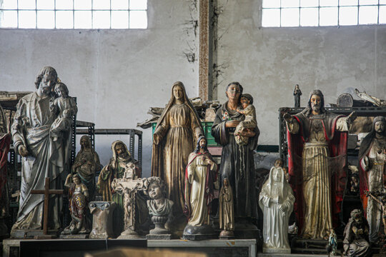 A number of statues of Jesus and the Virgin Mary are displayed in an old gallery.