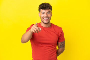 Young caucasian handsome man isolated on yellow background surprised and pointing front