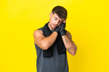 Young sport caucasian man with towel isolated on yellow background making sleep gesture in dorable...