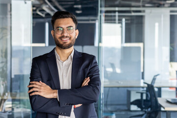 Fototapeta premium Confident mature man businessman posed in a office setting with arms folded. The image exudes professionalism, confidence, and ambition, making it ideal for business or leadership-related contexts.