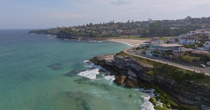 Cinematic reveal aerial view of Bronte Beach in Sydney, Australia, showing turquoise ocean water, golden sand, rolling waves, and scenic Pacific coastal landscapes in a smooth motion.