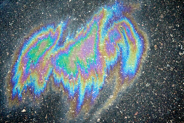 Colorful gasoline or oil spill on asphalt creating rainbow sheen reflecting light