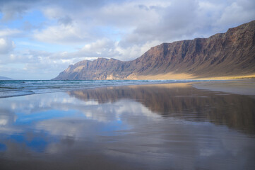 Stunning view of Famara beach with the reflection of the cliff during low tide, Lanzarote, Canary islands, Spain
