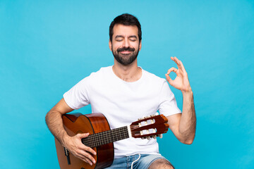 Young man with guitar over isolated blue background in zen pose