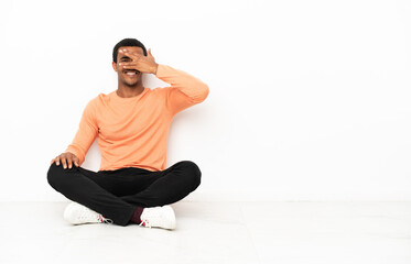 Fototapeta premium African American man sitting on the floor over isolated copyspace background covering eyes by hands and smiling