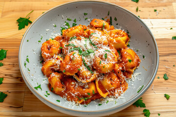 A vibrant top-down shot of tortellini pasta coated in rich tomato sauce, topped with fresh parsley and sprinkled Parmesan cheese on a rustic wooden table.