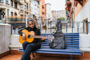 Young latin woman playing acoustic guitar outdoors