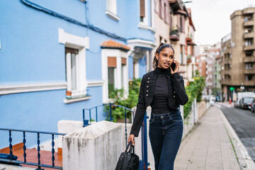 Young latin woman walking on the sidewalk and talking on smartphone