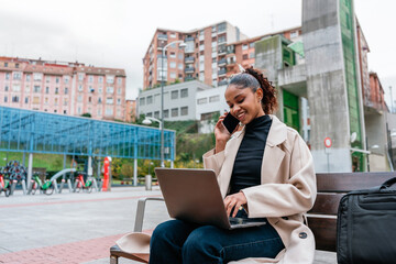 Young latin businesswoman working remotely in the city using laptop and smartphone