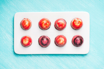 Assorted multi-colored homemade chocolates. Modern hand-painted chocolates on a white plate on a blue background. copyspace.Product concept for chocolatier. Selected focus.