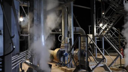 White steam escaping from a leaking pipe in an industrial setting at night underscores potential hazards and safety issues related to pressure and emissions. Heavy industry concept. Chemical and