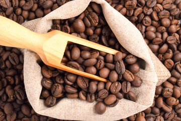 Roasted coffee beans in a sack with a wooden scoop. Top view