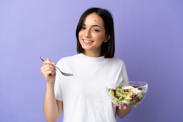 Young caucasian woman isolated on purple background holding a bowl of salad with happy expression