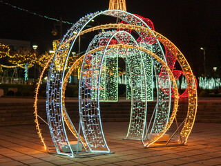 Colorful arches adorned with bright lights create a festive atmosphere in a winter park. People enjoy the enchanting display amid twinkling lights and holiday decorations.