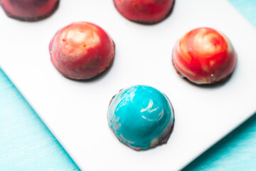 Assorted multi-colored homemade chocolates. Modern hand-painted chocolates on a white plate on a blue background. copyspace.Product concept for chocolatier. Selected focus.
