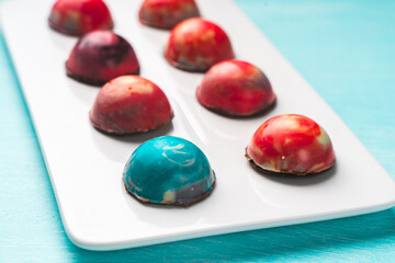 Assorted multi-colored homemade chocolates. Modern hand-painted chocolates on a white plate on a blue background. copyspace.Product concept for chocolatier. Selected focus.