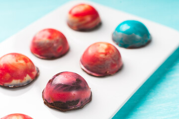 Assorted multi-colored homemade chocolates. Modern hand-painted chocolates on a white plate on a blue background. copyspace.Product concept for chocolatier. Selected focus.