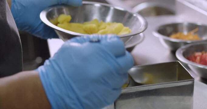 hands wearing blue gloves putting a layer of mashed potato during the preparation of Peruvian Causa